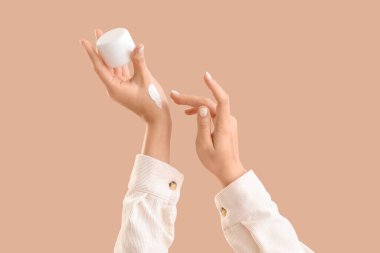 Bej arka planda bir kavanoz nemlendirici krem ile kadın elleri