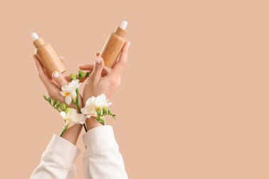 Bej arka planda kozmetik ürünleri ve çiçeklerle dolu kadın elleri