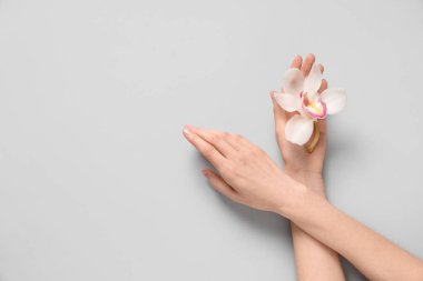 Gri arkaplanda orkide çiçeği olan güzel kadın elleri.