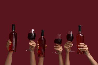 Koyu kırmızı arka planda bardakları ve şarap şişelerini tutan kadın eller.
