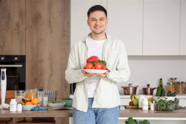 Yakışıklı genç adam mutfakta taze sebzeli tabak tutuyor. Sağlıklı gıda konsepti