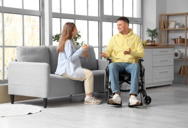 Tekerlekli sandalyedeki genç adam evde kız arkadaşıyla konuşuyor.