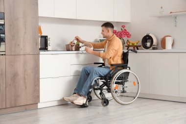 Tekerlekli sandalyedeki genç adam evde yemek yapıyor.