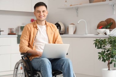 Evde dizüstü bilgisayar kullanan tekerlekli sandalyedeki yakışıklı genç adam.