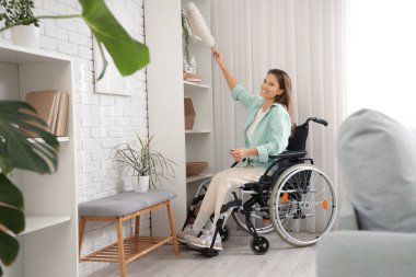 Tekerlekli sandalyedeki genç kadın evinde toz bezi ile temizlik yapıyor.