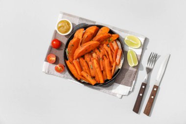 Lezzetli pişirilmiş tatlı patates, sos, domates, limon dilimleri ve gri arka planda çatal bıçak takımı.