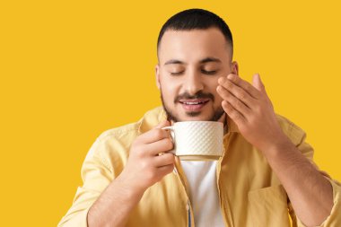 Sarı arka planda seramik bardaklı genç adam, yakın plan.