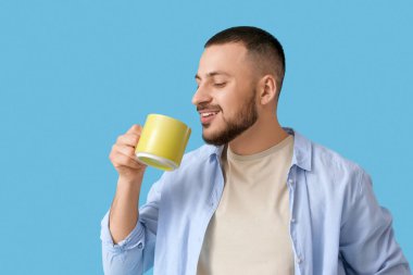 Mavi arka planda sarı seramik bardaklı genç adam.