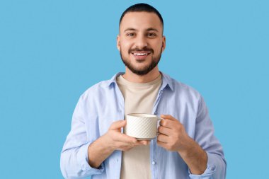 Mavi arka planda seramik bardaklı genç adam.