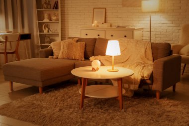 Rahat bir kanepe, kahve masası ve oturma odasının içinde parlayan lambalar.