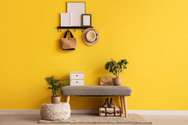 Bankta, kancalarda ve çiçeklerde sarı duvarın yanında.