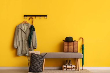 Sarı duvarda paltosu ve şemsiyesi olan sırık ve kancalar.