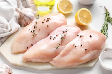 Çiğ tavuk göğsü ve beyaz arka planda farklı baharatlar olan tahta.