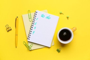 Yapılacaklar listesi boş bir defter, sarı arka planda bir fincan kahve ve kırtasiye. Üst görünüm