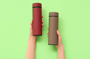 Yeşil arka planda farklı modern termoslara sahip kadın elleri.
