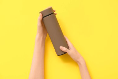 Sarı arka planda modern kahverengi termoslu kadın elleri.