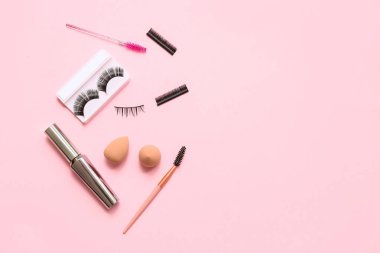 Farklı takma kirpikler, fırçalar, rimel ve pembe arka planda süngerler.