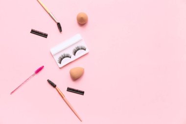 Farklı takma kirpiklerle pembe arka planda fırçalar ve süngerler.