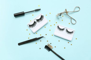 Mavi arka planda fırça, cımbız ve bigudiyle farklı takma kirpikleri var.