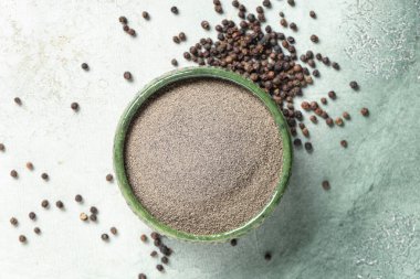 Arkaplanda karabiber tozu ve karabiber olan bir kase.