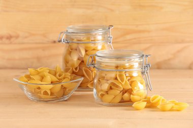 Kavanoz ve cam kase, ahşap zemin üzerinde çiğ koni makarna.