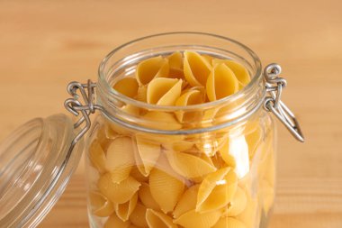 Ahşap arka planda çiğ koni makarnalı kavanoz, yakın plan.