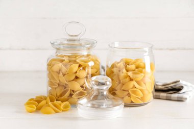 Beyaz ahşap arka planda çiğ koni makarnalı kavanozlar.