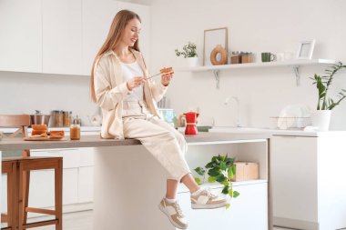 Genç bir kadın mutfakta bıçakla fıstık ezmesi sürüyor.