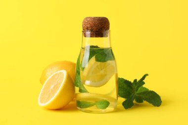 Sarı zemin üzerinde limon ve nane yaprakları olan bir kavanoz su.