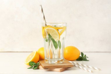 Limonlu bir bardak su, arka planda nane yaprakları ve pipetler