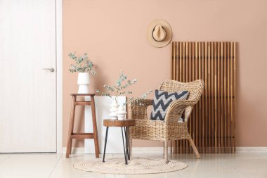 Hasır koltuk ve okaliptüs dallı kahve masası bej duvarın yanındaki vazolarda.