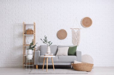 Raflama ünitesi, rahat kanepe ve okaliptüs dalları beyaz tuğla duvarın yanındaki odalarda.