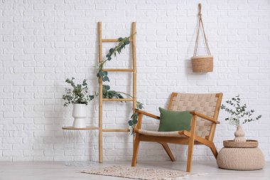 Hasır koltuk, merdiven ve okaliptüs dallı kahve masası. Odada beyaz tuğla duvarın yanında.