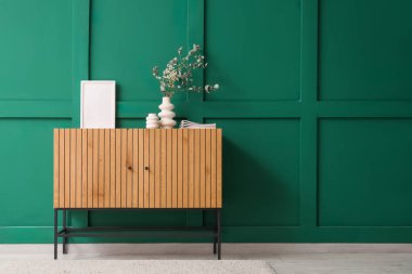 İçinde dekor ve okaliptüs dalları olan çekmeceler yeşil duvarın yanındaki vazoda.