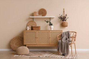 Hasır sandalye ve çekmeceler içinde okaliptüs dalları olan bir vazo. Odadaki bej duvarın yanında.