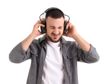 Young man in headphones suffering from loud noise on white background clipart