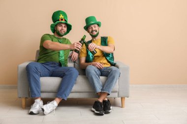 Yeşil sakallı, leprikon şapkalı genç adamlar ellerinde bira şişeleri ve bej duvarın yanındaki kanepede oturuyorlar. Aziz Patrick Günü kutlaması