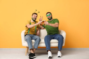 Yeşil sakallı yonca şeklinde gözlüklü genç adamlar ellerinde bira kupaları ve sarı duvarın yanındaki kanepede oturuyorlar. Aziz Patrick Günü kutlaması