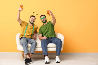 Yeşil sakallı yonca şeklinde gözlüklü genç adamlar ellerinde bira kupaları ve sarı duvarın yanındaki kanepede oturuyorlar. Aziz Patrick Günü kutlaması