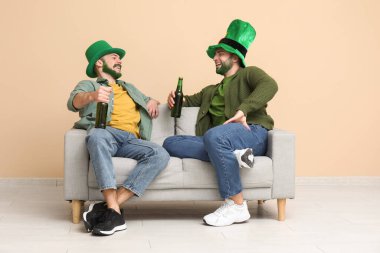 Yeşil sakallı, leprikon şapkalı genç adamlar ellerinde bira şişeleri ve bej duvarın yanındaki kanepede oturuyorlar. Aziz Patrick Günü kutlaması
