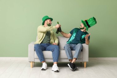 Yeşil sakallı, leprikon şapkalı genç adamlar ellerinde bira şişeleri ve yeşil duvarın yanındaki kanepede oturuyorlar. Aziz Patrick Günü kutlaması