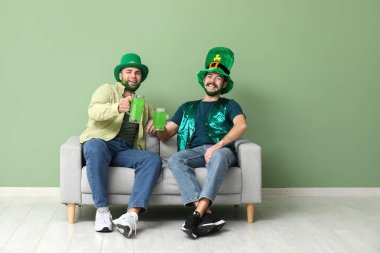 Yeşil sakallı, leprikon şapkalı genç adamlar ellerinde bira bardakları ve yeşil duvarın yanındaki kanepede oturuyorlar. Aziz Patrick Günü kutlaması