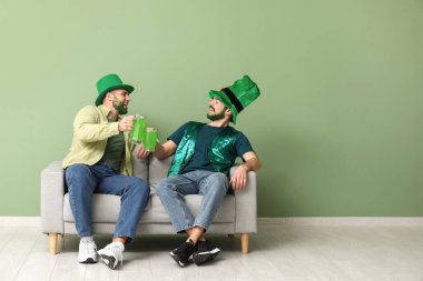 Yeşil sakallı, leprikon şapkalı genç adamlar ellerinde bira bardakları ve yeşil duvarın yanındaki kanepede oturuyorlar. Aziz Patrick Günü kutlaması