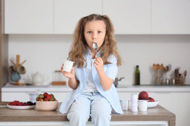 Mutfaktaki masada elinde yoğurt paketi ve kaşıkla oturan tatlı küçük kız.