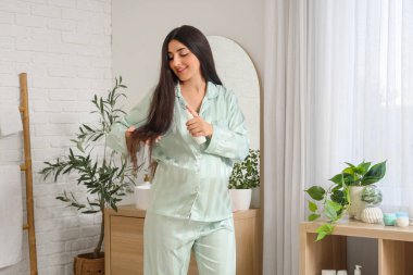 Genç hamile bir kadın banyoda saç bakım ürünleri kullanıyor.