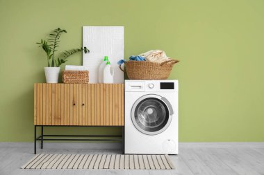 Çamaşır sepetinin, çamaşır makinesinin ve ahşap dolabın olduğu odanın içi.