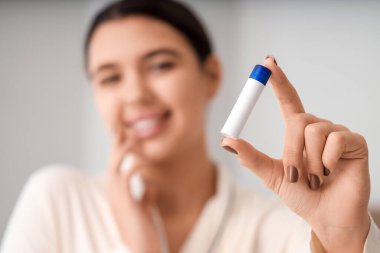 Young woman with lip balm at home, closeup clipart