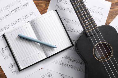 Ahşap arka planda Ukulele, defter, kalem ve nota kağıtları, yakın plan