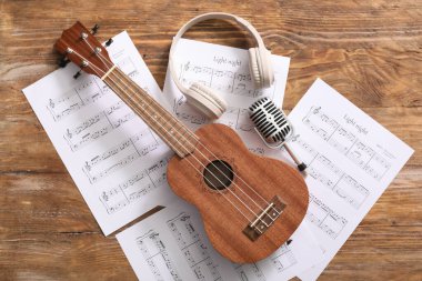 Ukulele, mikrofon, müzik kağıtları ve ahşap arka planda kulaklıklar