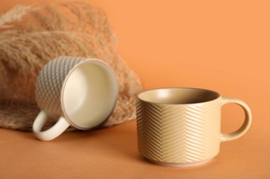 Turuncu arka planda kuru sazlıklar olan farklı seramik kupalar.